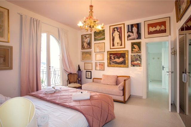 Schlafzimmer im Château de l’Anglais mit Doppelbett, Sofa, Kronleuchter und Gemälden, Bogenfenster zum Balkon