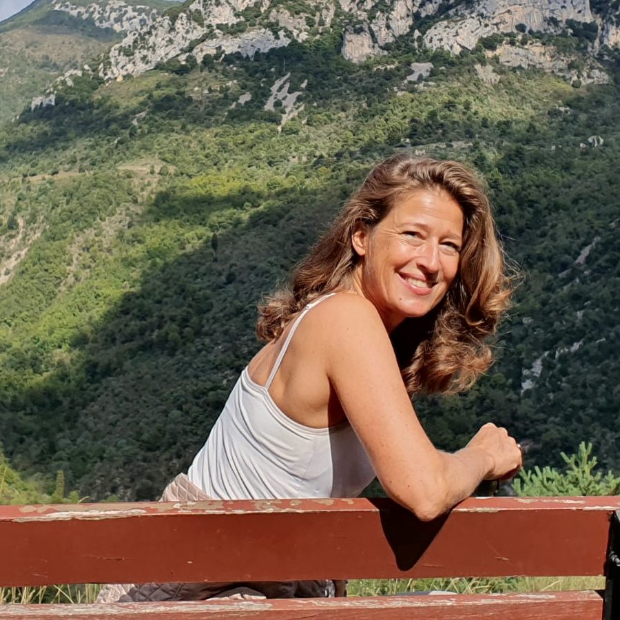 Gesa Kaehlbrandt assise sur un banc au-dessus de la vallée, les pentes boisées des baous derrière elle