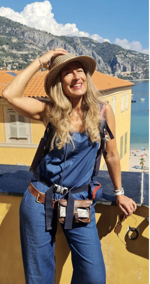 Gesa Kaehlbrandt auf einer Terrasse über Menton, mit Strohhut und Rucksack, dahinter das Meer und die Hänge der Küste