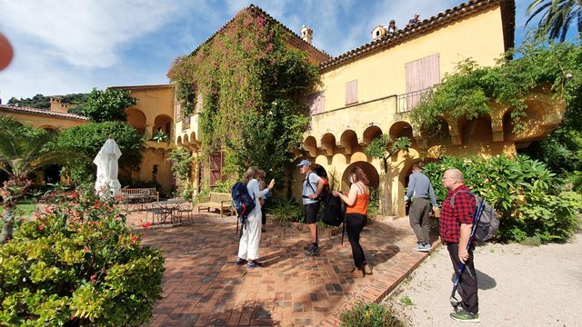 Wandergruppe vor einer ockerfarbenen Villa mit Arkaden und Garten am Boulevard Garavan